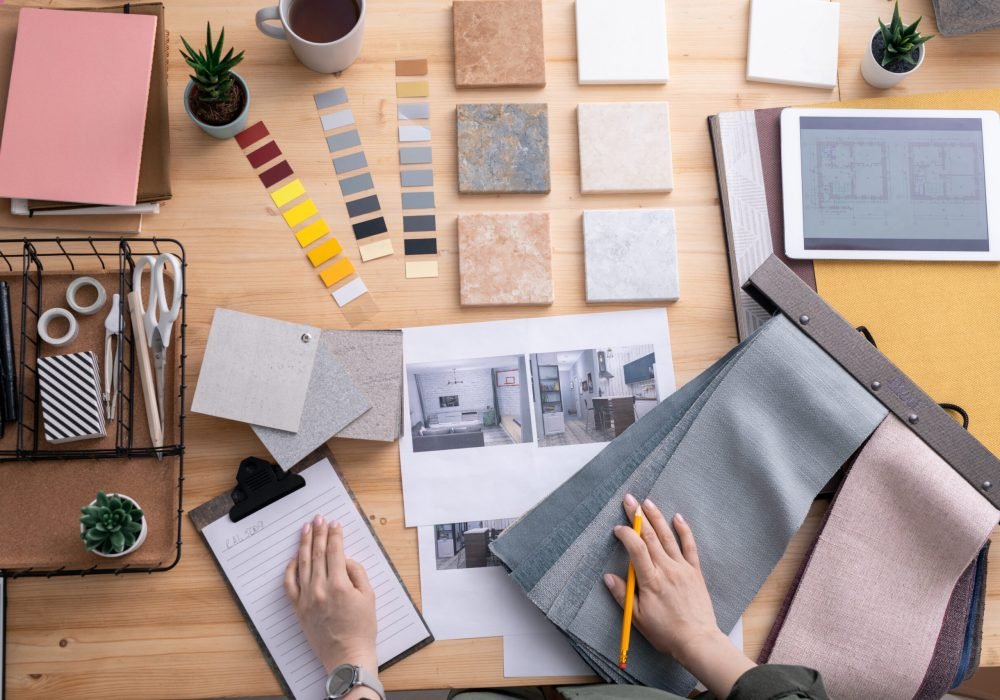 Flat lay of hands of contemporary creative interior designer over workplace during work over new apartment or room in house